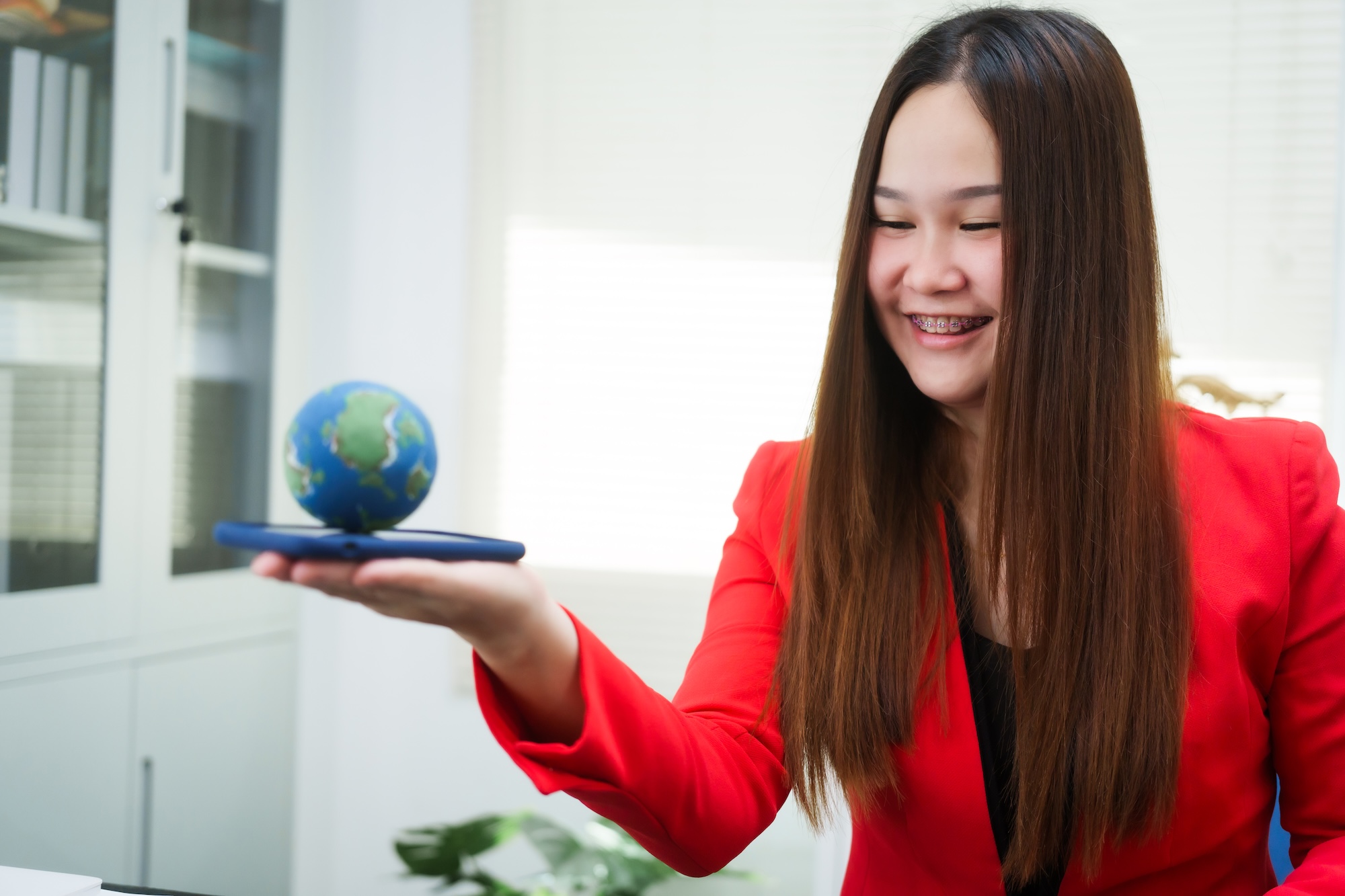 a young, smiling businesswoman holds a globe her desk, symbolizing global environmental awareness